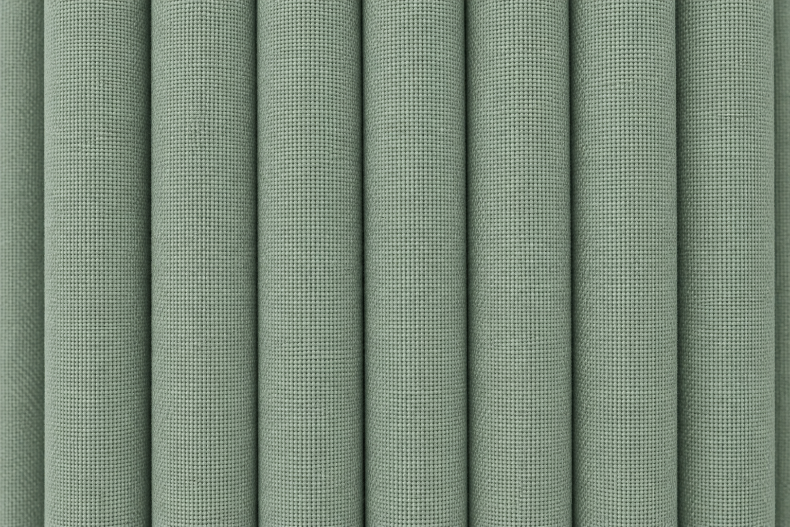 A close-up of vertically pleated fabric in a muted sage green color, showing the woven texture and soft shadows between the folds.